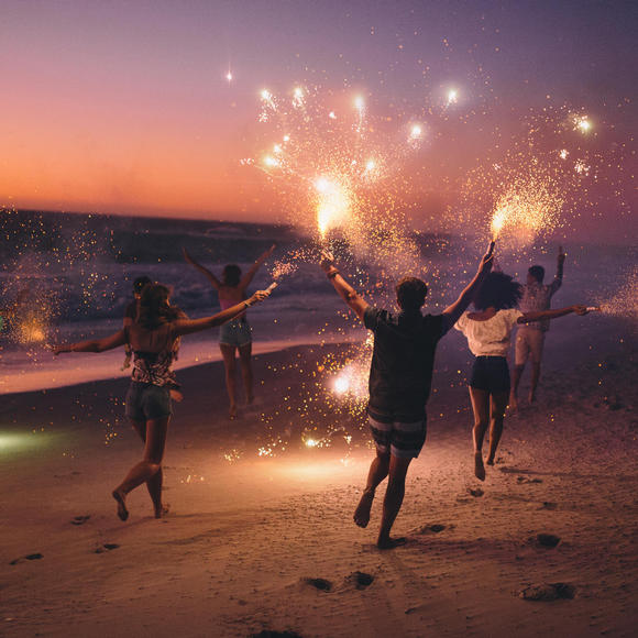 Group of people dancing and holding sparklers on beach